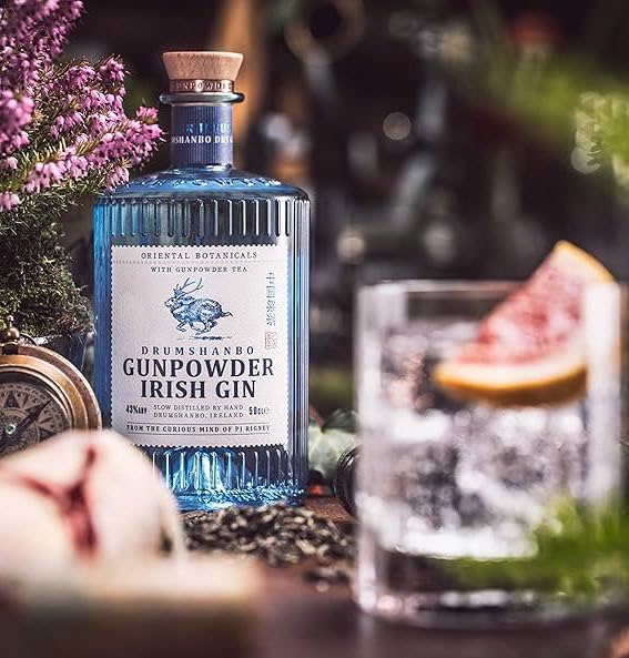 An image of a bottle of Drumshanbo Gunpowder Irish Gin, next to a delicious cocktail. Beautiful blue bottle that standout from the rest. 