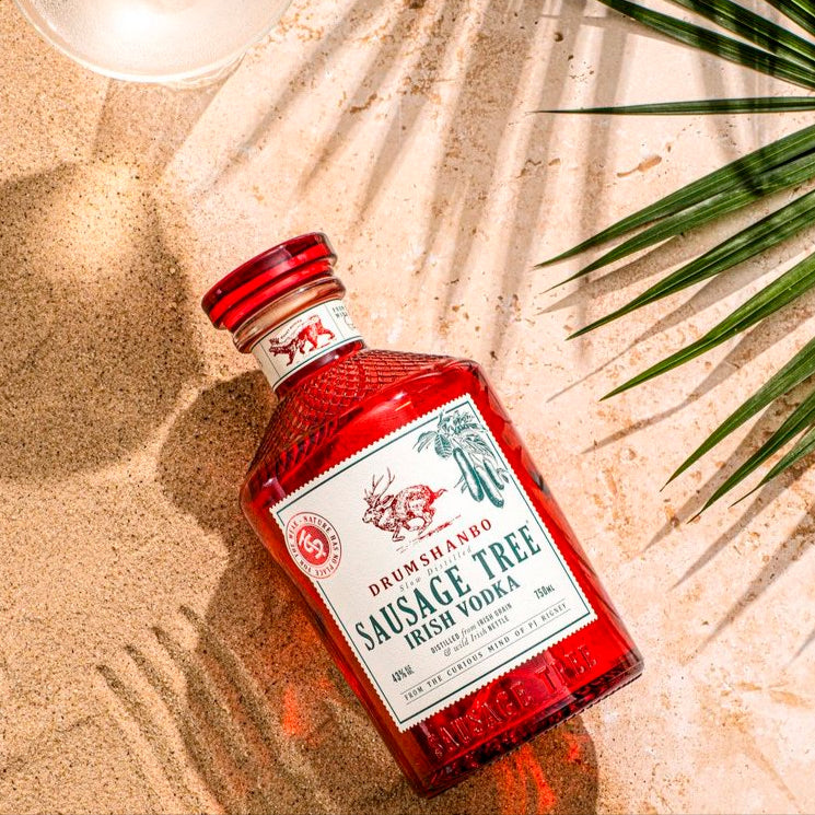 Load image into Gallery viewer, Bottle of Drumshanbo Sausage Tree Irish Vodka on a sandy surface with palm leaves.