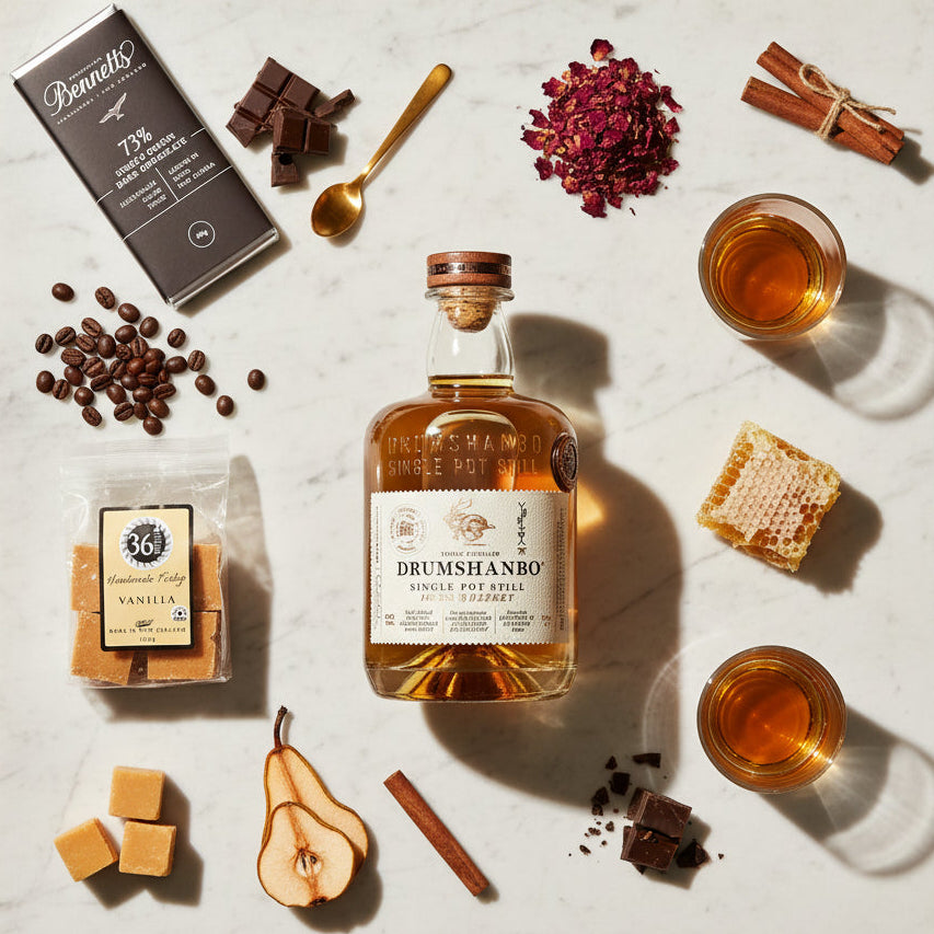 Load image into Gallery viewer, A bottle of Drumshanbo Single Pot Still Irish Whiskey is arranged on a white marble board with autumn and caramel-themed ingredients, including a bag of 36 Degrees Vanilla fudge, a Bennetts dark chocolate bar, cinnamon sticks, dried rosebuds, coffee beans, honeycomb, pears, and two glasses of the amber whiskey.