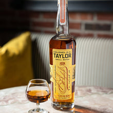 Load image into Gallery viewer, Bottle of Colonel E.H. Taylor whiskey with a glass on a marble surface, with a blurred background.