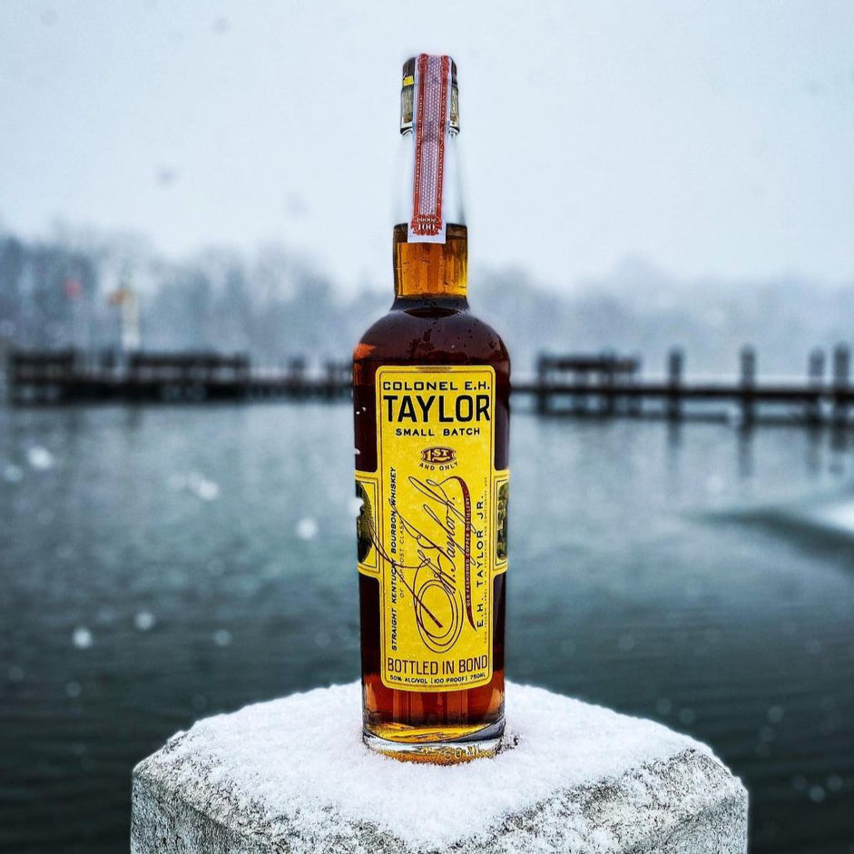 Load image into Gallery viewer, Bottle of Colonel E.L. Taylor bourbon on a snowy surface with a blurred background.