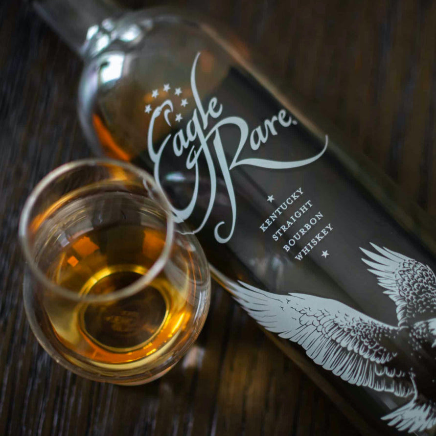 Load image into Gallery viewer, Bottle and glass of Eagle Rare Kentucky Straight Bourbon Whiskey on a wooden surface.