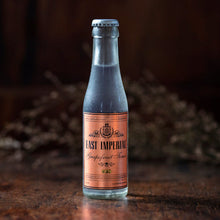 Load image into Gallery viewer, A bottle of East Imperial Grapefruit Tonic on a wooden surface with a dark background