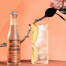 Load image into Gallery viewer, Bottle of East Imperial Grapefruit tonic water with a glass of cocktail and peach slice on a peach background