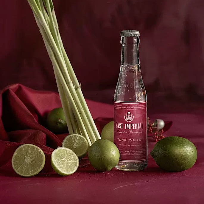 Load image into Gallery viewer, Bottle of East Imperial Tonic Water with limes and lemongrass on a red fabric background
