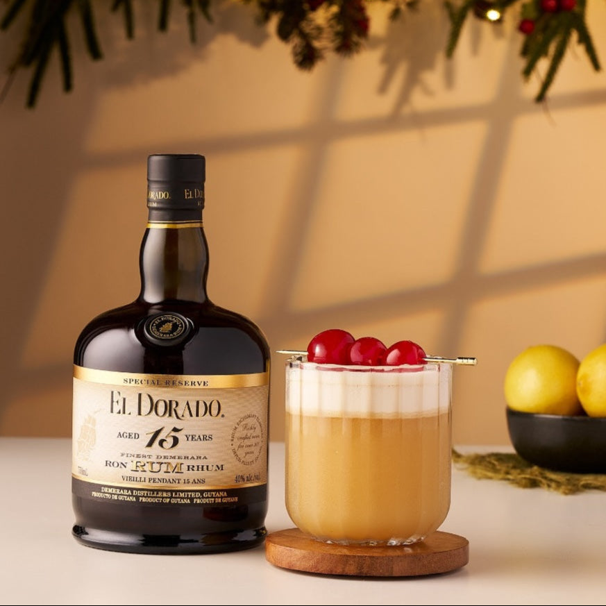 Load image into Gallery viewer, El Dorado 15YO rum bottle with a cocktail garnished with cherries on a table.