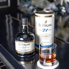 Load image into Gallery viewer, El Dorado 21-year-old rum bottle, can, and glass on a reflective surface with blurred background