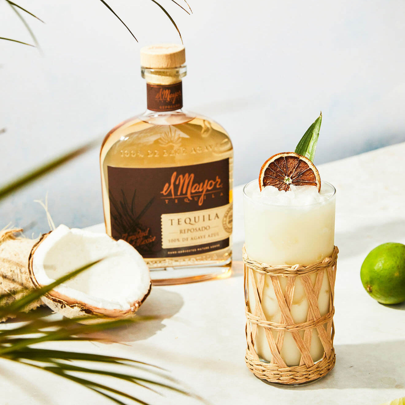 Load image into Gallery viewer, El Mayor Reposado Tequila bottle with a cocktail garnished with lime and coconut on a light background