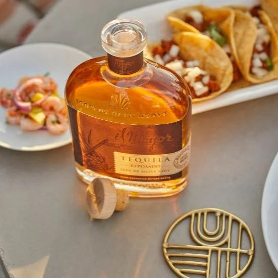 A bottle of El Mayor Reposado Tequila on a table with tacos and guacamole.