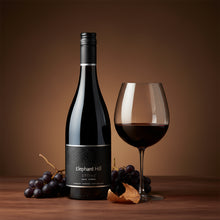 Load image into Gallery viewer, Elephant Hill STONE Syrah wine bottle and glass with grapes on a wooden surface and brown background