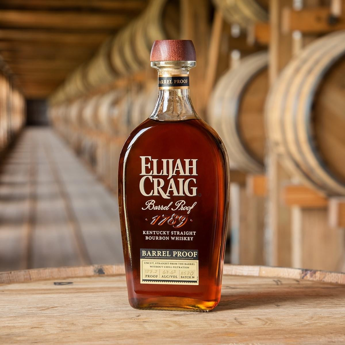 Load image into Gallery viewer, Bottle of Elijah Craig whiskey on a wooden surface with barrels in the background