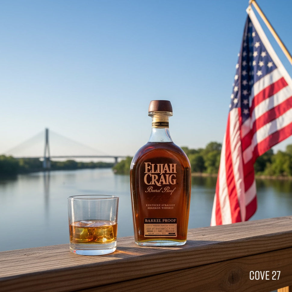 Load image into Gallery viewer, Bottle of Elijah Craig BOURBON whiskey with a glass on a wooden ledge by a body of water and American flag.