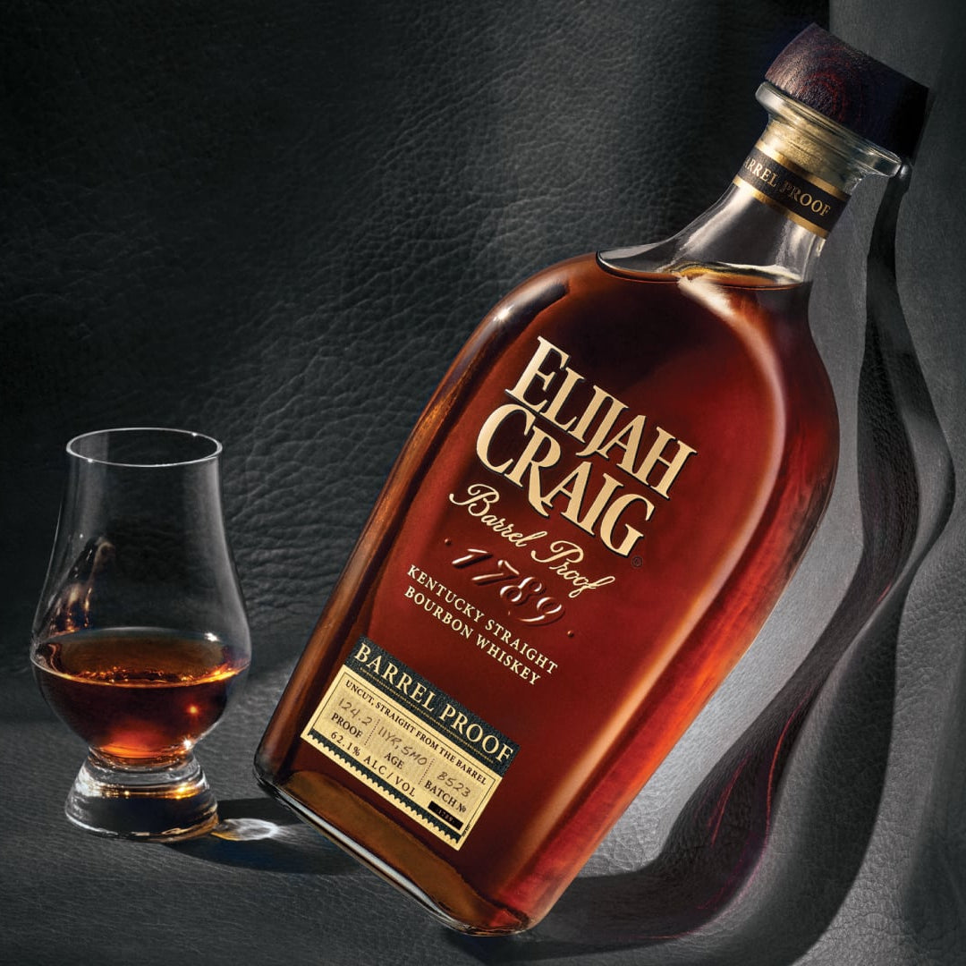 Load image into Gallery viewer, Bottle and glass of Elijah Craig bourbon on a dark background
