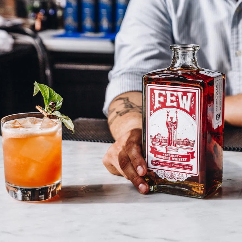 Load image into Gallery viewer, Person holding a bottle of 'FEW' whiskey with a cocktail on a table.