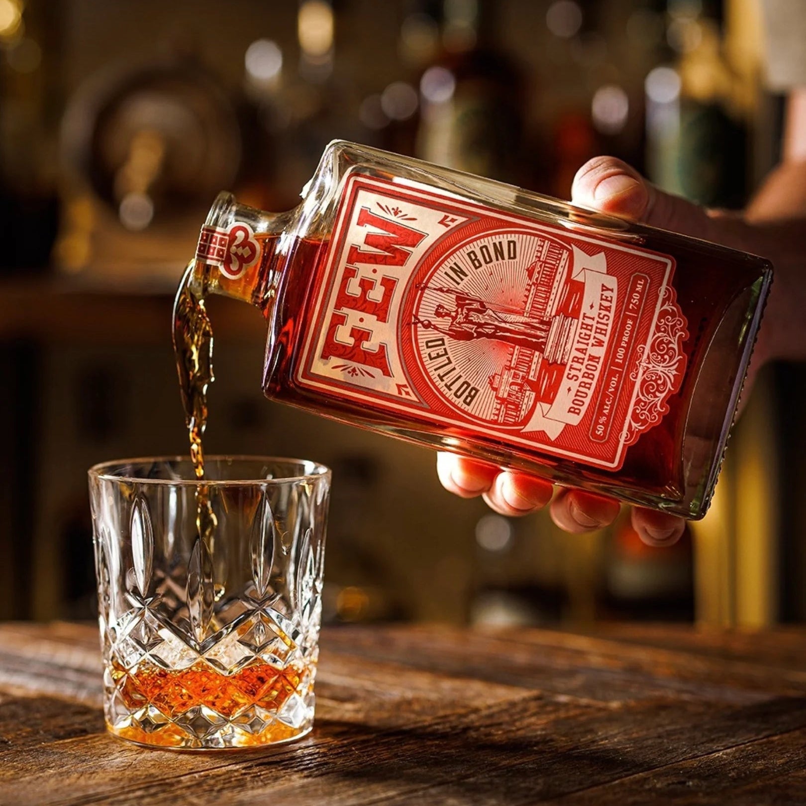 Load image into Gallery viewer, Hand pouring whiskey from a 'FEW' bottle into a glass on a wooden surface.