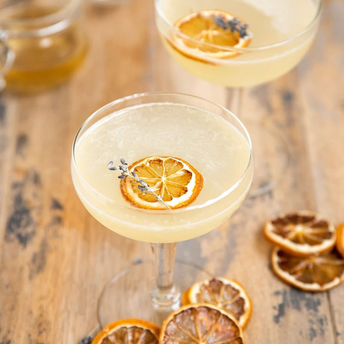 Load image into Gallery viewer, Two cocktails with dried lemon slices and lavender on a wooden surface