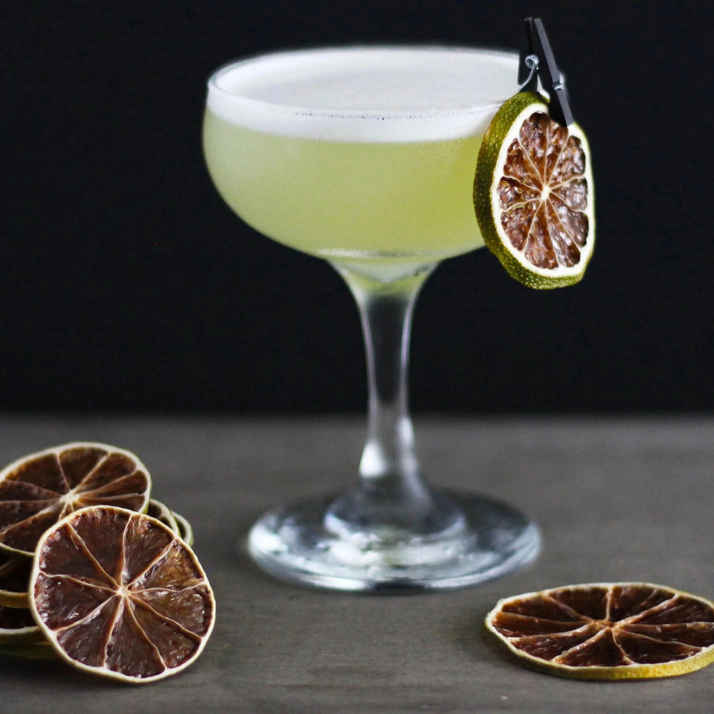 Cocktail in a glass with a lime wheel garnish on a dark surface.