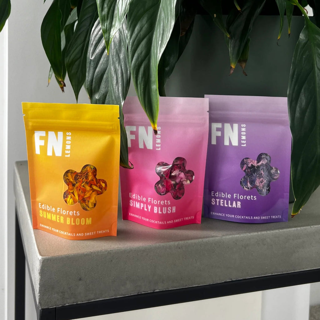 Three colourful packages of dried edible flower florets labeled 'FN Lemon' on a surface with green leaves in the background
