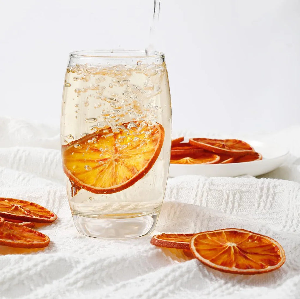 Glass of sparkling water with dried orange slices on a white surface