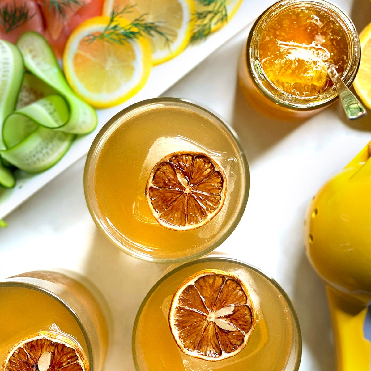 Load image into Gallery viewer, Three cocktails from above with orange garnish slices on a white surface with lemons and limes.