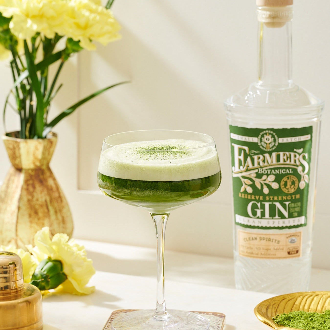 Load image into Gallery viewer, Green cocktail in a glass with a bottle of Farmers Botanical Gin on a white surface with flowers.