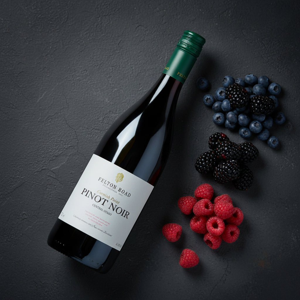 Load image into Gallery viewer, A bottle of Felton Road Cornish Point Pinot Noir red wine is arranged diagonally on a dark textured surface, surrounded by fresh berries including raspberries, blackberries, and blueberries.