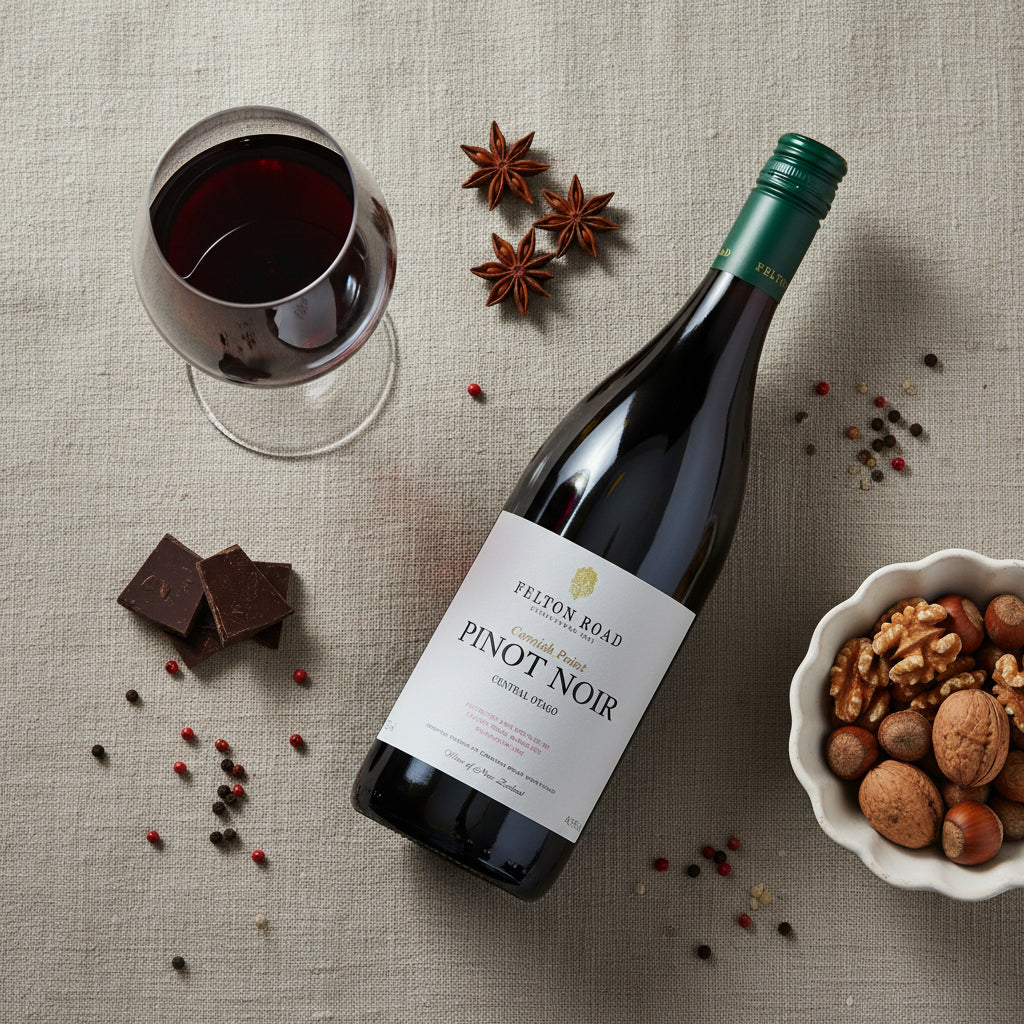 Load image into Gallery viewer, A bottle of Felton Road Cornish Point Pinot Noir red wine with a glass of red wine, chocolate pieces, star anise, peppercorns, and a bowl of walnuts and hazelnuts on a textured linen surface.