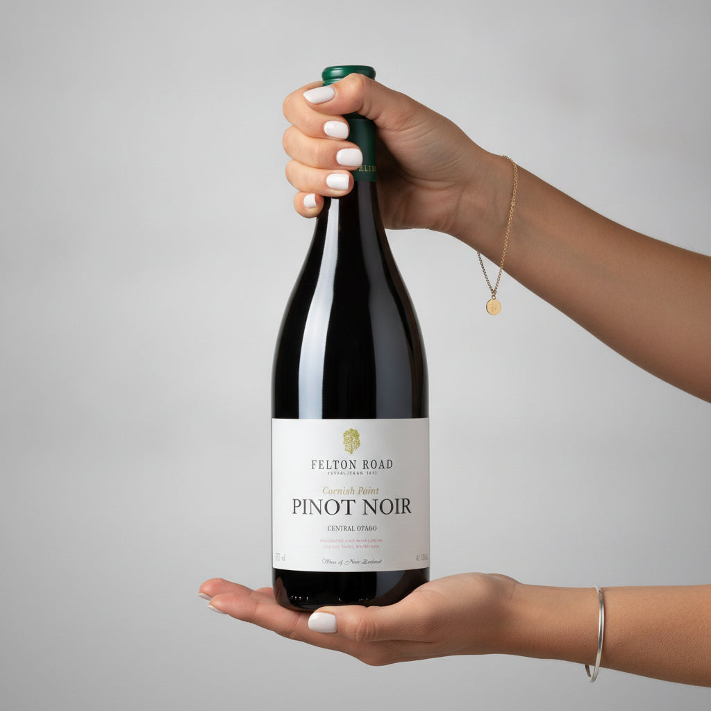 Load image into Gallery viewer, Women hands holding a bottle of Felton Road Cornish Point Pinot Noir red wine against a neutral grey background, with another hand supporting the base of the bottle.