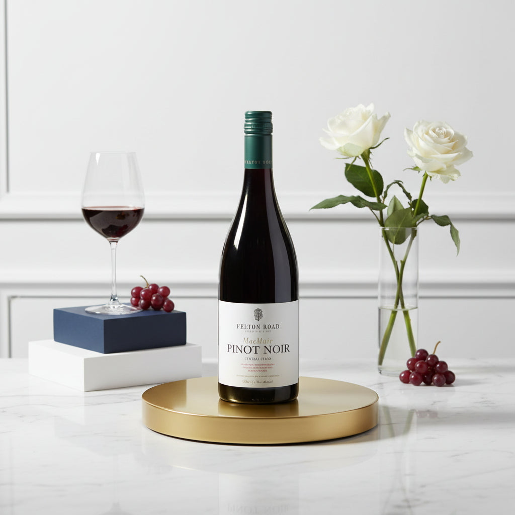 Load image into Gallery viewer, A bottle of Felton Road MacMuir Pinot Noir red wine is displayed on a gold round tray, flanked by a glass of red wine, grapes, and white roses on a white marble surface against a white panelled wall.