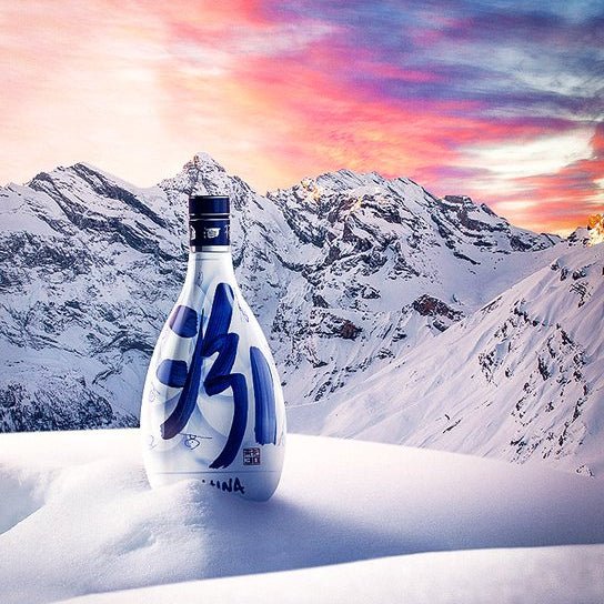 Bottle with blue design in a snowy landscape with mountains and a colorful sky.