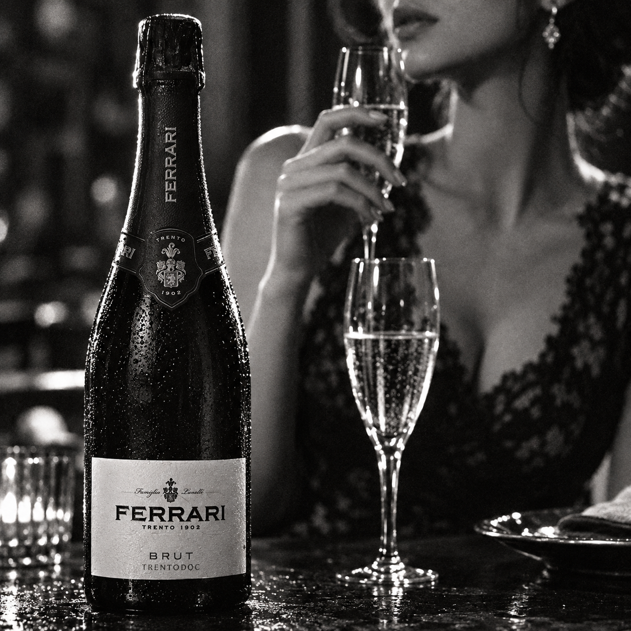 Load image into Gallery viewer, A bottle of Ferrari Brut Trentodoc sparkling wine stands on a table beside two filled champagne flutes, with a woman in a dark lace dress holding one glass in a dimly lit bar setting.