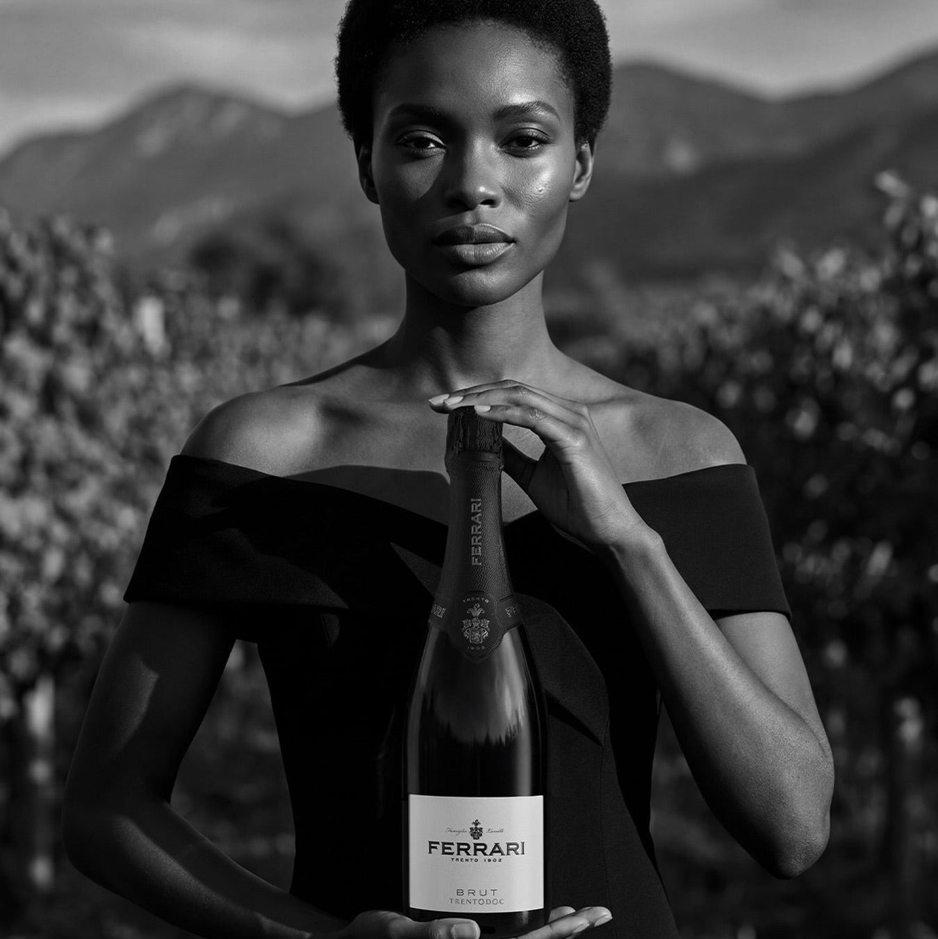 Load image into Gallery viewer, Woman holding a Ferrari Trento Brut Metodo Classico sparkling wine bottle with a scenic background