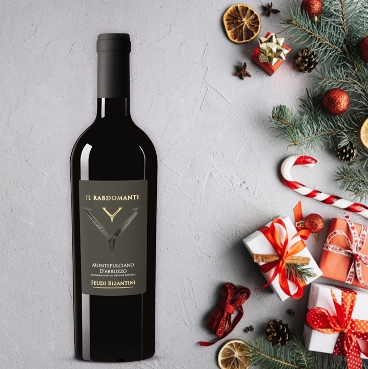 Load image into Gallery viewer, A bottle of Feudi Bizantini Il Rabdomante Montepulciano next to Christmas gifts and tree branches