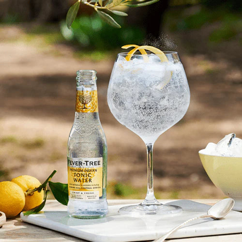 Load image into Gallery viewer, Fever-Tree Indian tonic water bottle with a glass of tonic and lemon on a table outdoors.
