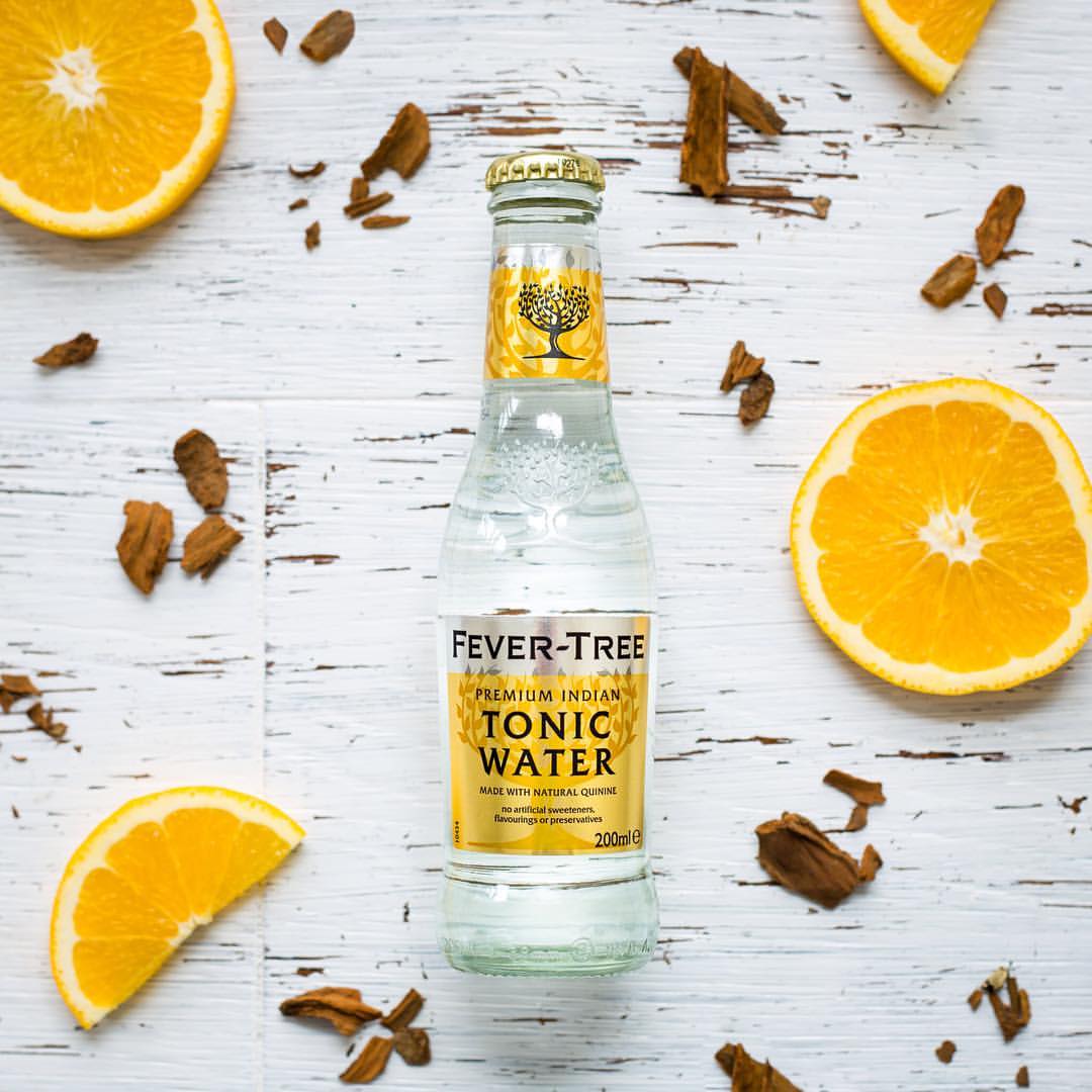 Load image into Gallery viewer, Fever-Tree Indian tonic water bottle with orange slices and cinnamon on a wooden surface