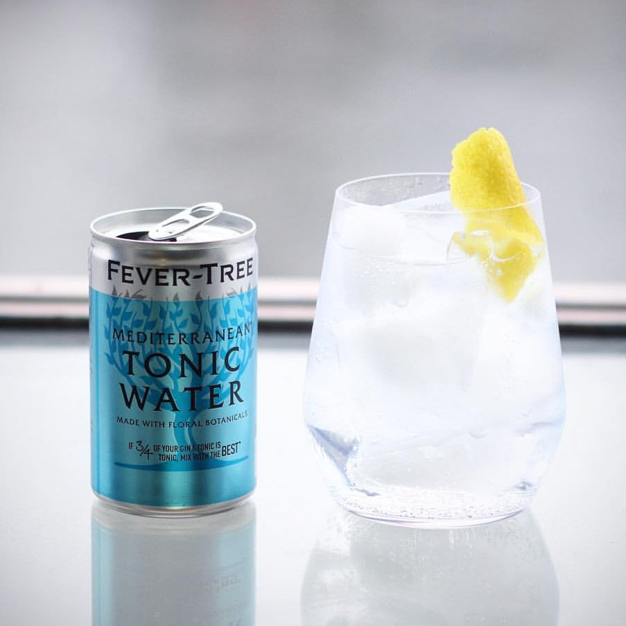 Load image into Gallery viewer, Fever-Tree Mediterranean tonic water can next to a glass of tonic water with a lemon twist on a reflective surface.