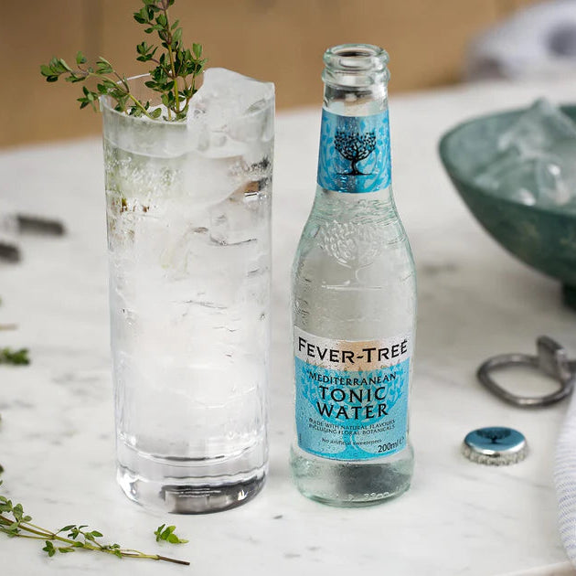 Load image into Gallery viewer, Fever-Tree Mediterranean tonic water bottle with a glass of tonic water and ice on a marble surface.