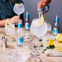 Load image into Gallery viewer, Person pouring Fever-tree Mediterranean tonic water into a glass with ice and other drinks on a marble surface.