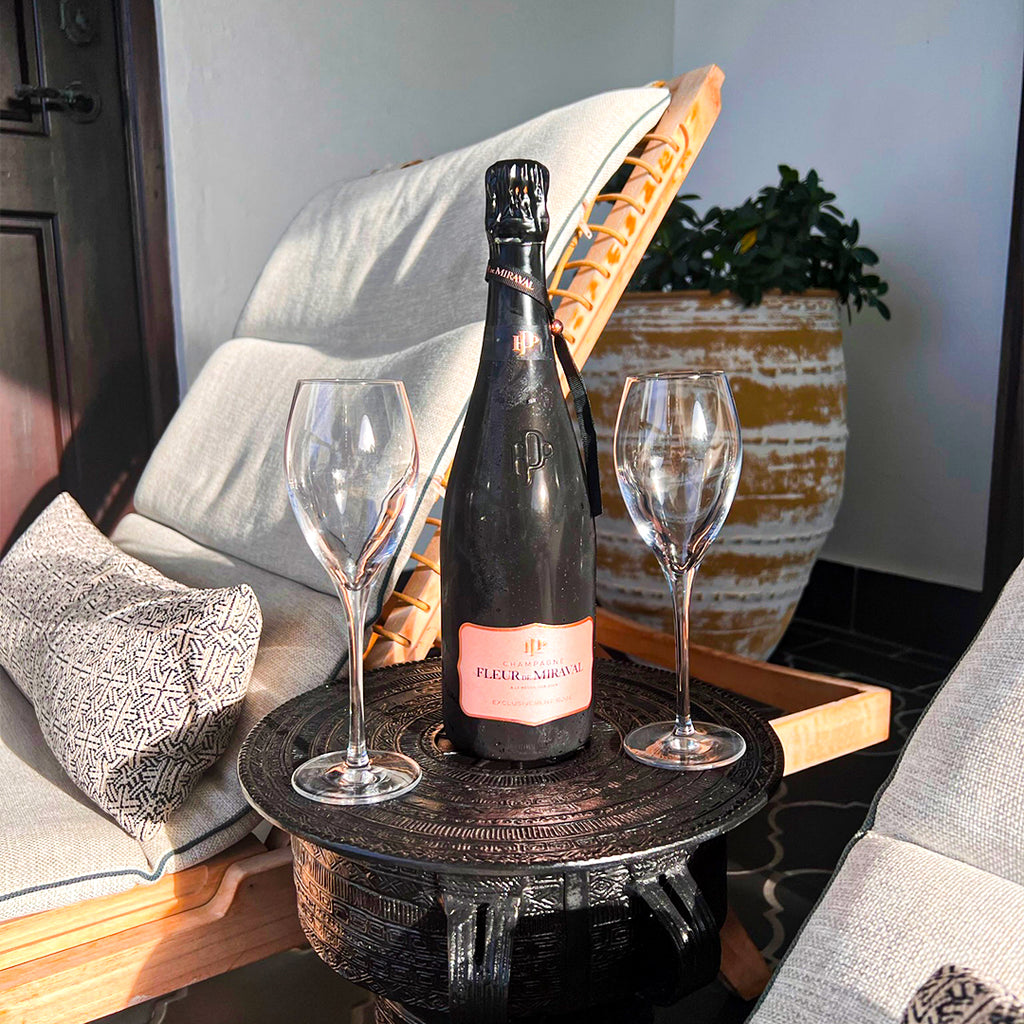 Bottle of Fleur de Champagne with two wine glasses on a small table outdoors.