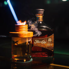 Load image into Gallery viewer, Bottle of Flor de Cana 18 year old Rum  with a lit candle and blue light in a dark setting