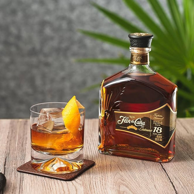 Bottle of Flor de Caña 18-year-old rum with a glass of cocktail on a wooden surface.