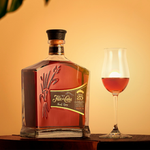 Load image into Gallery viewer, Bottle of Flor de Cana 25 year old Rum with a glass of red wine on an orange background