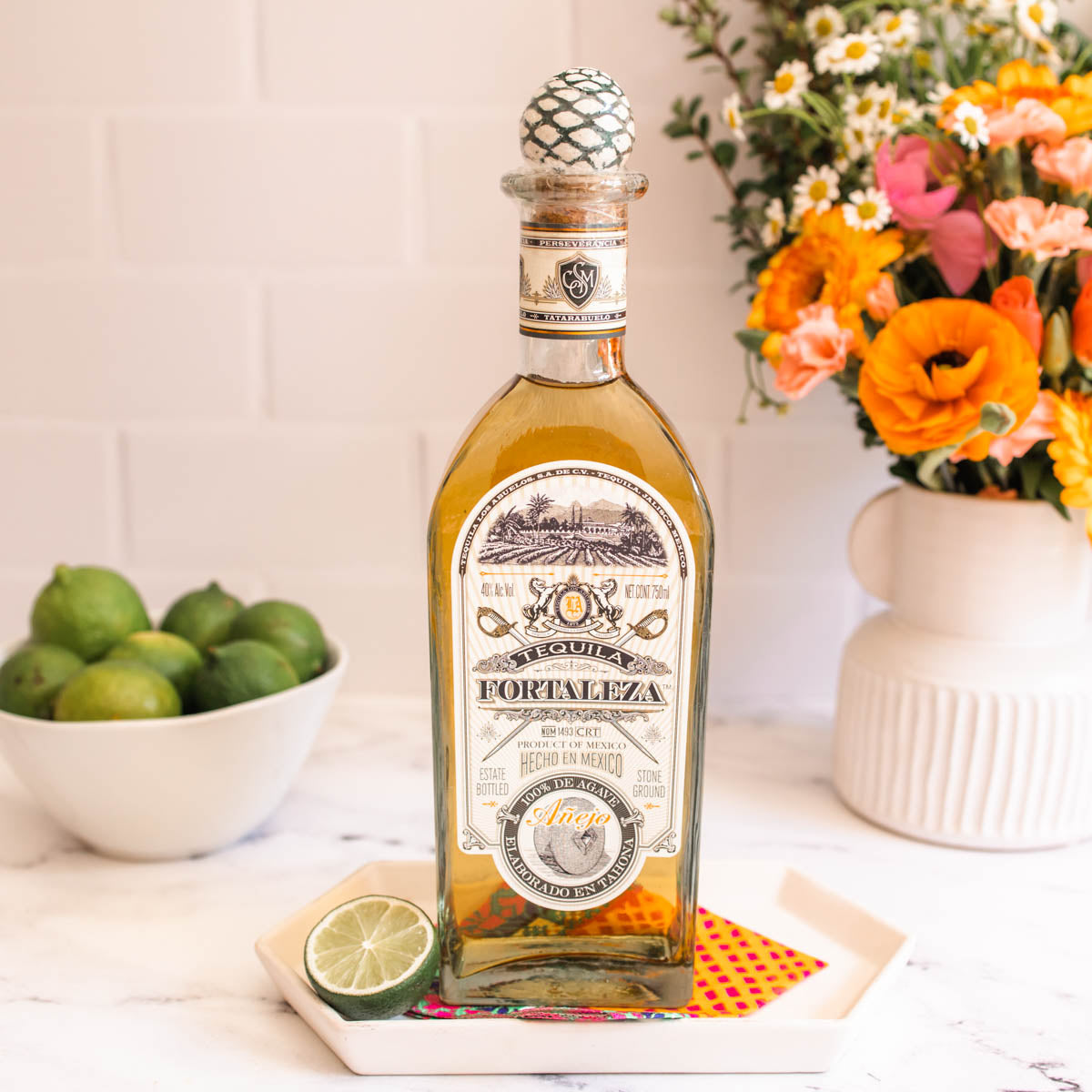 Load image into Gallery viewer, Bottle of Fortaleza tequila with limes and flowers on a table