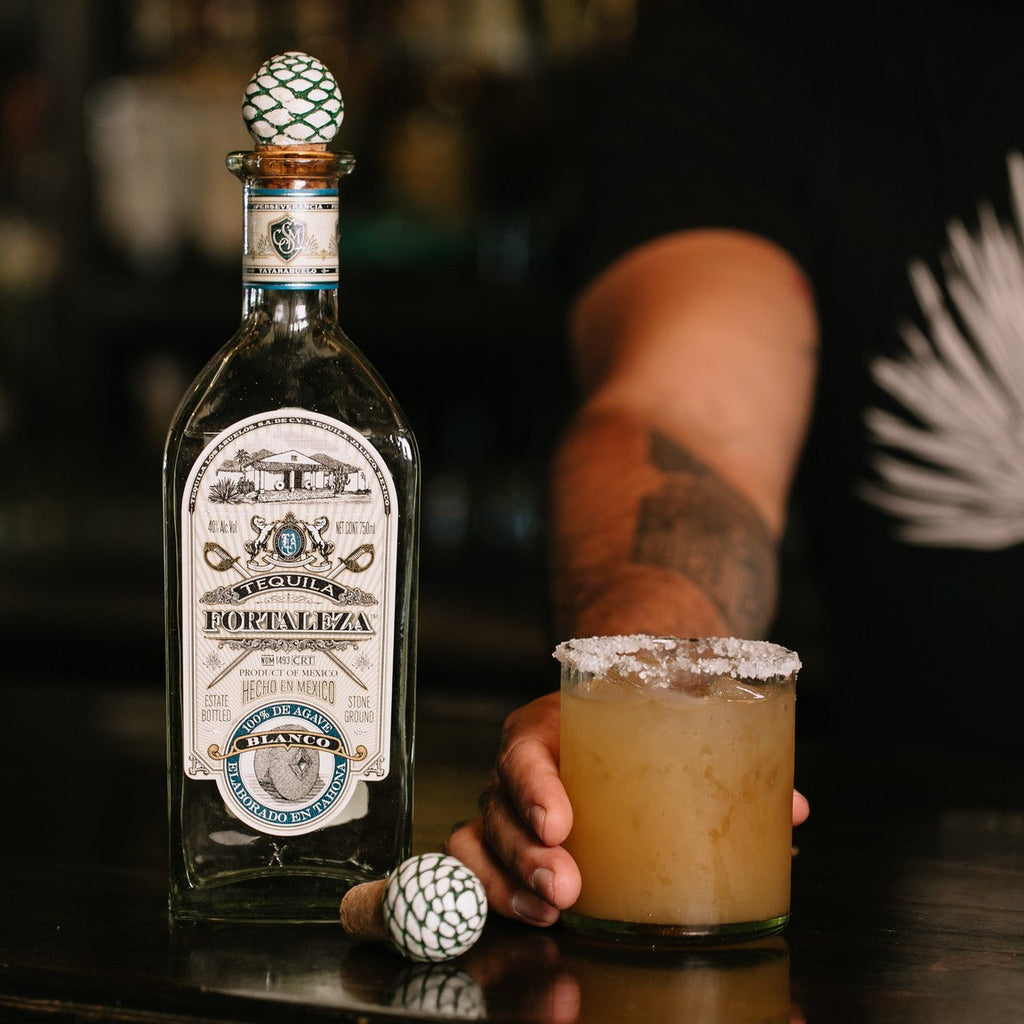 Fortaleza Blanco Tequila bottle with a margarita on a bar counter, blurred background