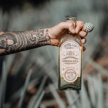 Load image into Gallery viewer, Person holding a bottle of Fortaleza Reposado tequila against a blurred natural background