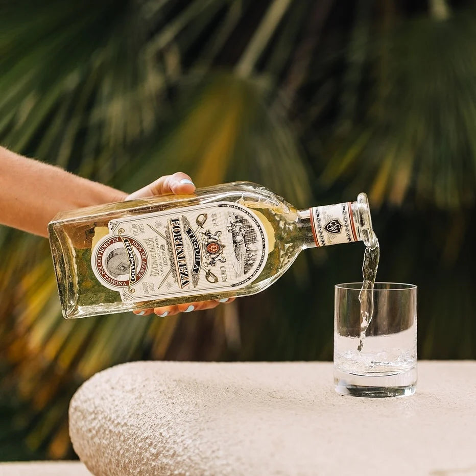 Load image into Gallery viewer, Hand pouring liquor from a bottle into a glass with a blurred green background