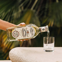 Load image into Gallery viewer, Hand pouring liquor from a bottle into a glass with a blurred green background