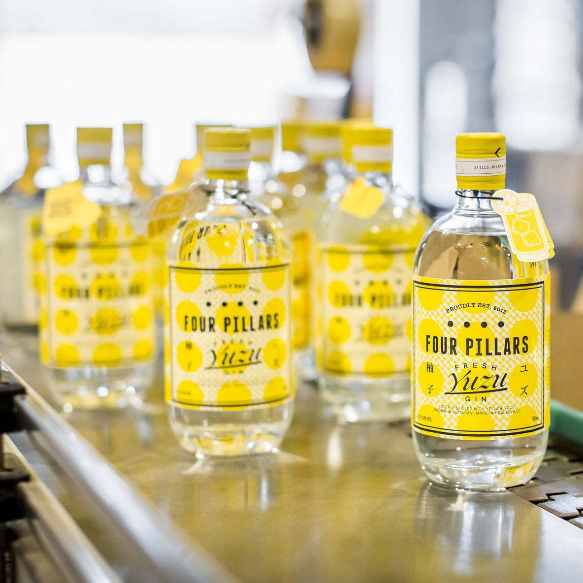 Load image into Gallery viewer, Bottles of Four Pillars Yuzu Gin on a production line with blurred background