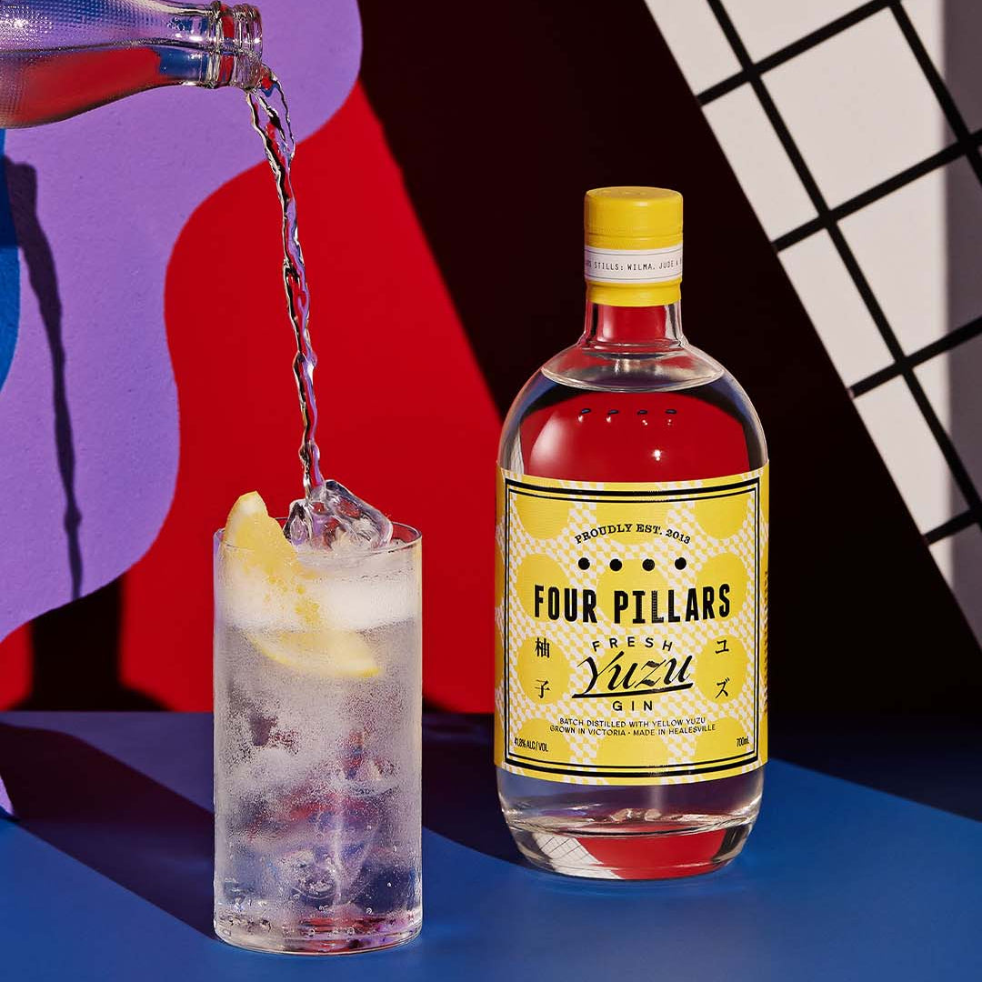 Load image into Gallery viewer, Four Pillars Yuzu Gin bottle with a cocktail being poured into a glass against a colorful background