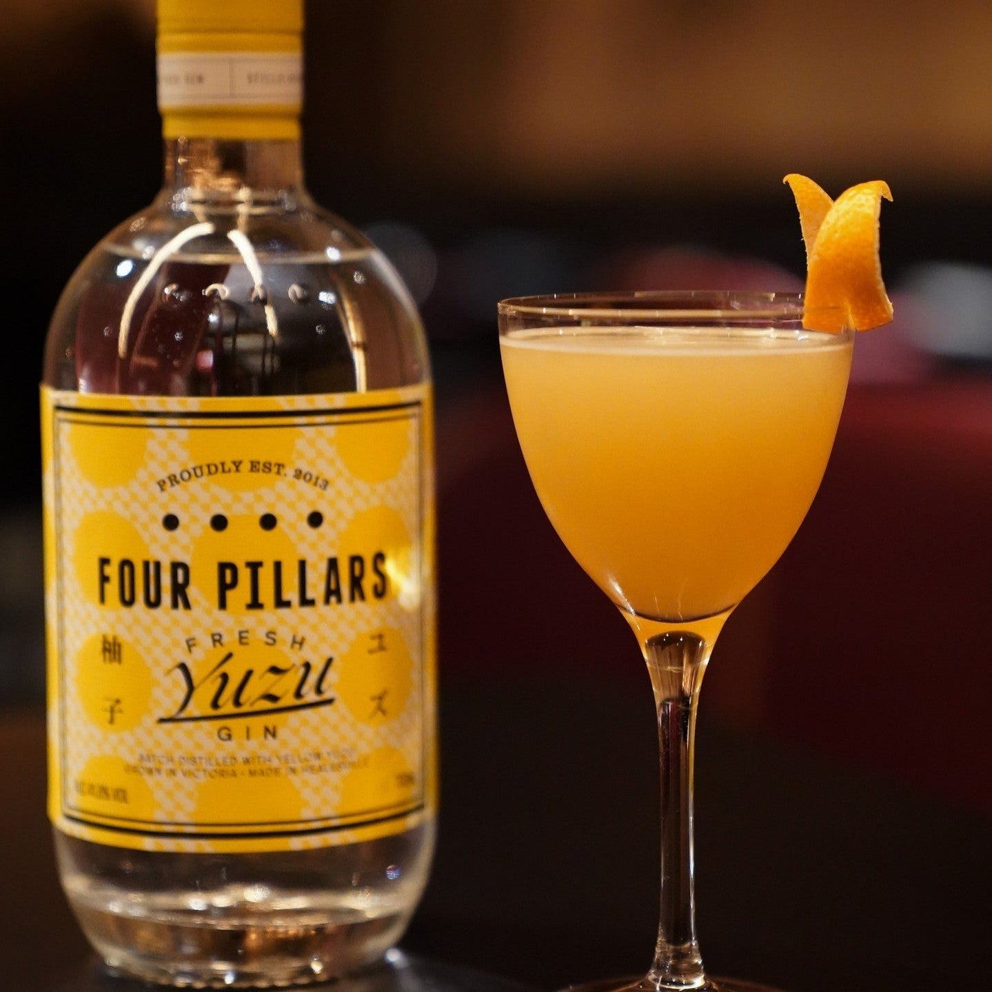 Load image into Gallery viewer, Four Pillars Fresh Yuzu gin bottle with a cocktail garnished with yuzu peel on a dark background